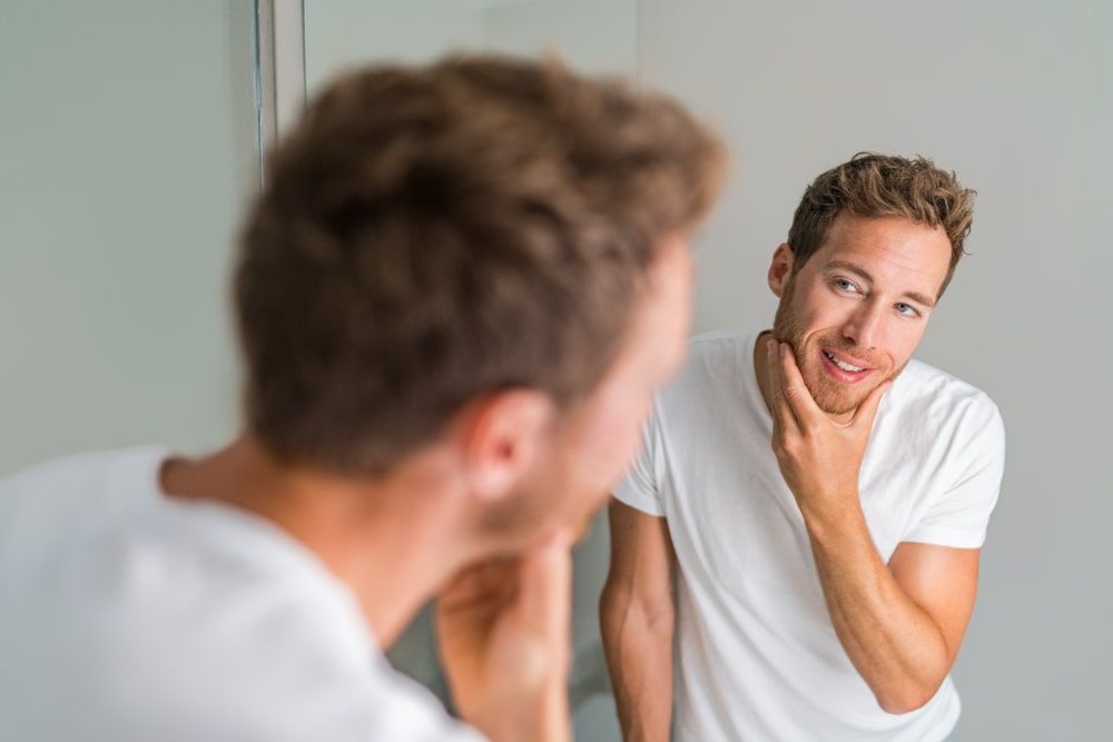 Male beauty young man touching beard and face looking in mirror