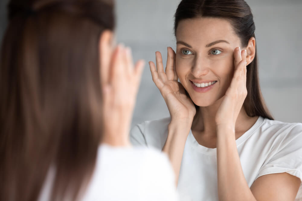 Attractive smiling young brunette woman looking at mirror