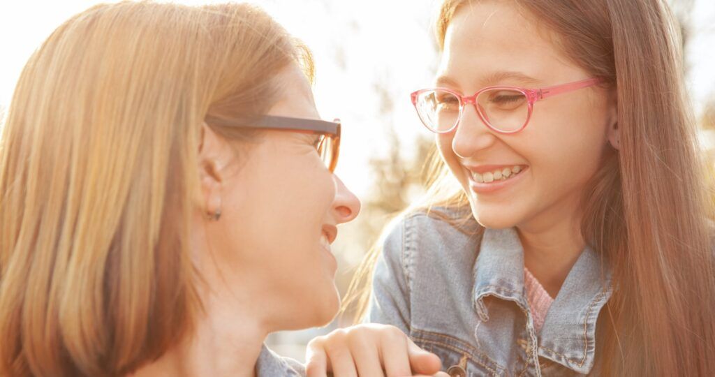 cute young girl wearing glasses, smiling at her mother outdoors