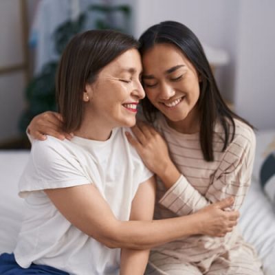 Two women mother and daughter hugging each other sitting on bed at bedroom