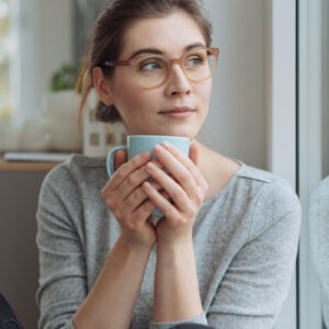 Serious young woman sitting daydreaming with mug