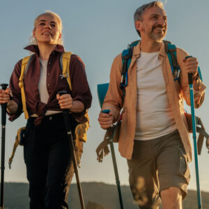 Hiking middle age couple follow trail along grassy mountain ridge