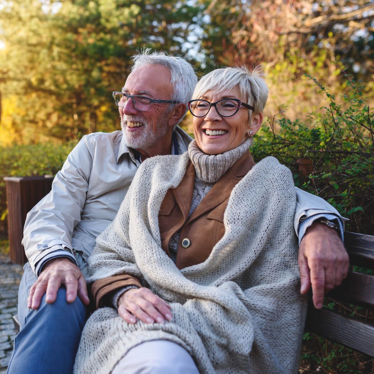 Smiling senior couple sitting on the bench in the park together enjoying retirement