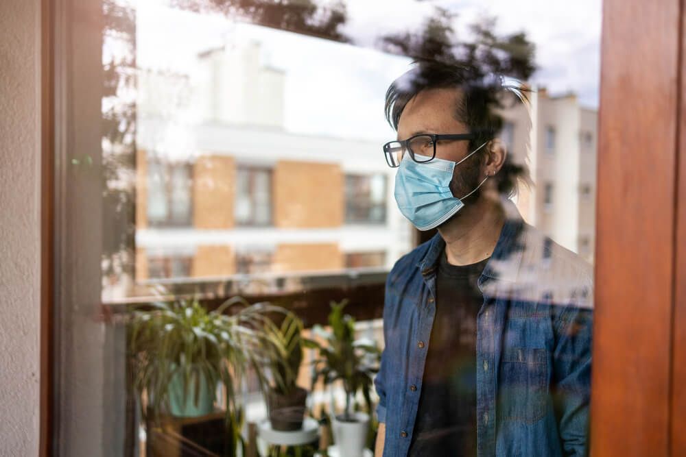 Man with face mask looking out of window