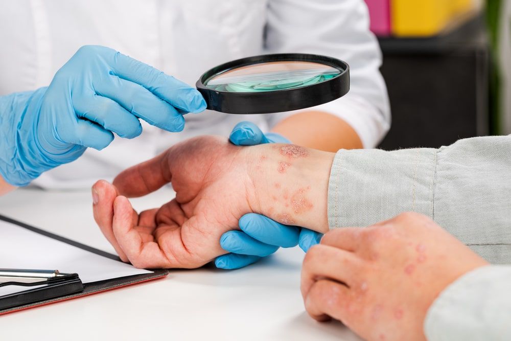 A dermatologist wearing gloves examines the skin of a sick patient.