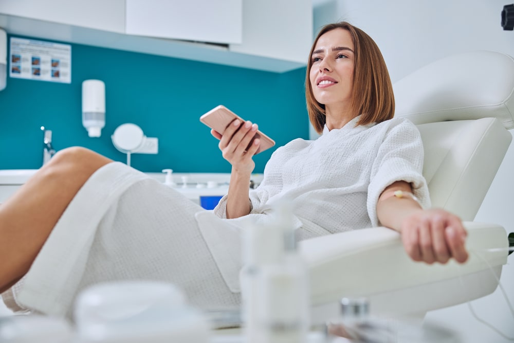 Beautiful elegant female sitting in armchair and getting intravenous vitamin drip treatment