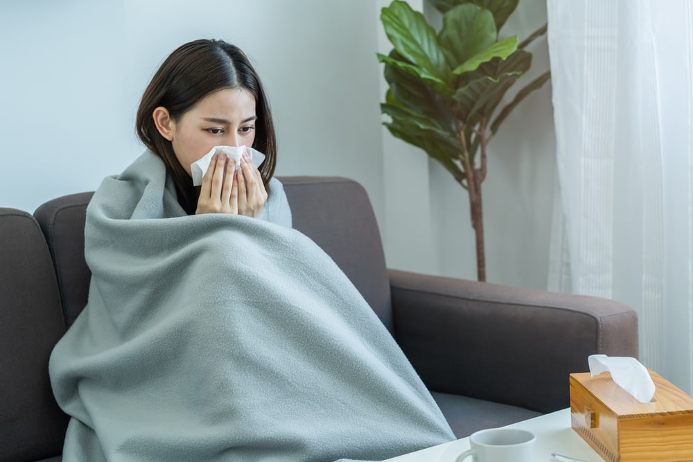 girl headache under blanket have a fever, flu and use tissues paper sneezing nose, runny sitting on sofa