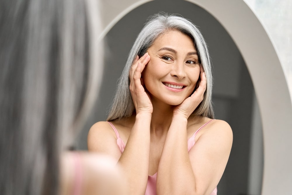 Happy middle aged woman with gray hair looking at mirror reflection