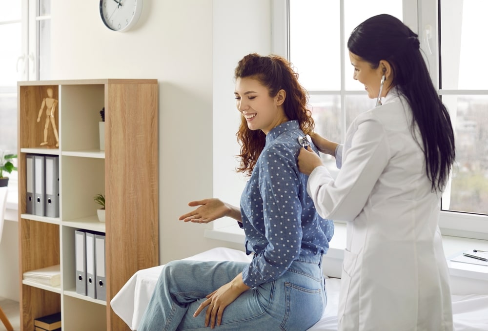 Nurse listens to female patient's back to check her lungs, breathing or heartbeat