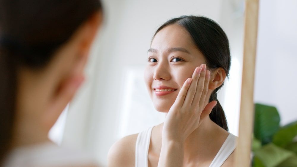 Young woman touching healthy facial beauty skin look at mirror