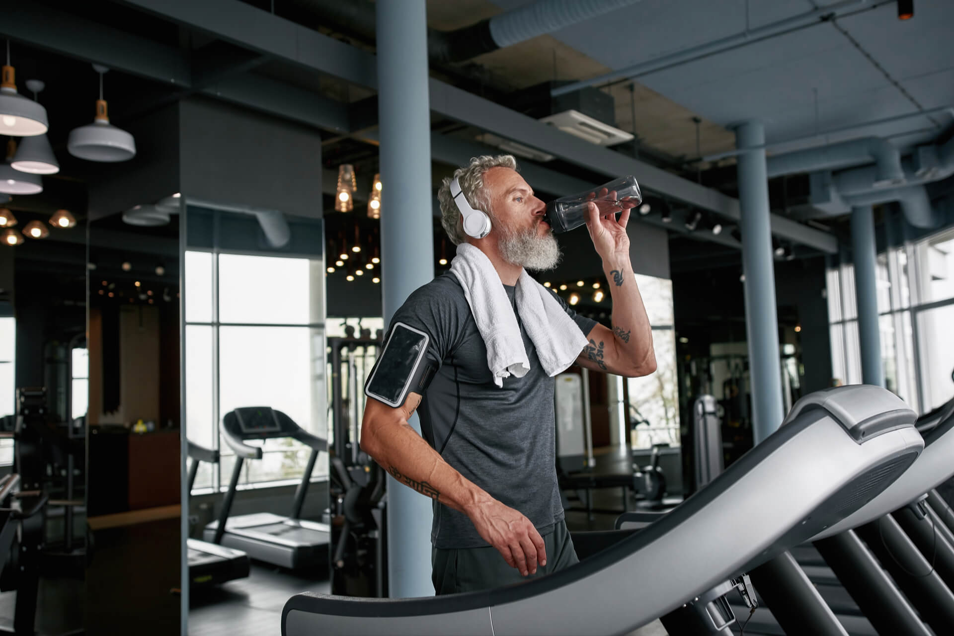 Active aged bearded man with towel around neck drinking water