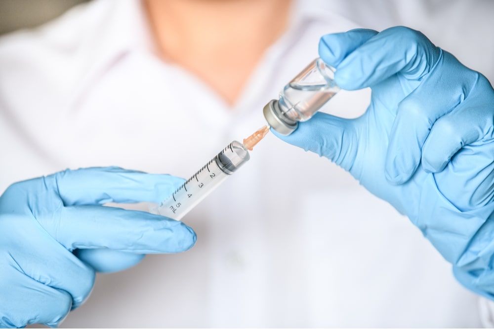hand in blue glove holding syringe with needle