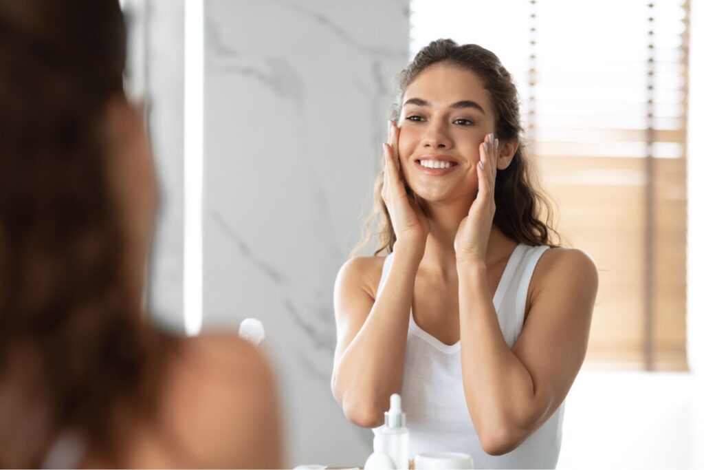 Woman Touching Smooth Face Skin Looking In Mirror In Bathroom