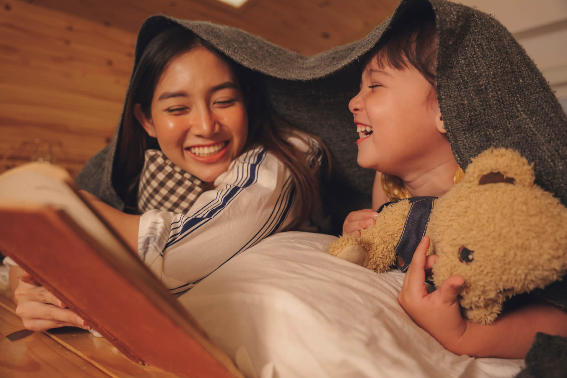 Asian mother and daughter read bed story book in bedroom at night.