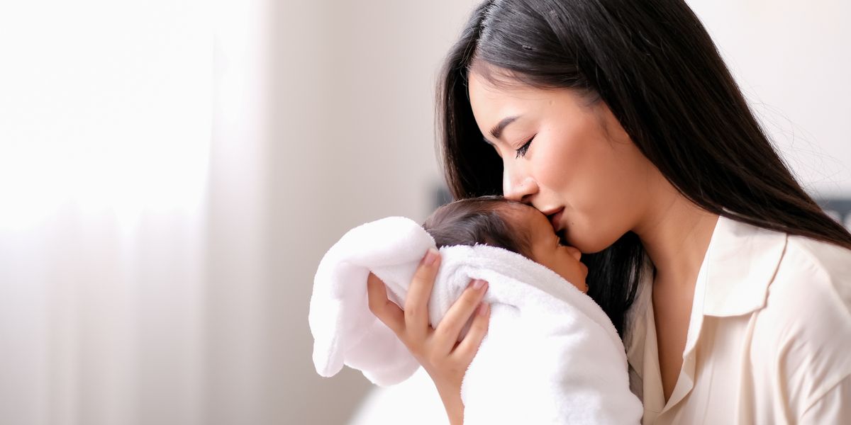 Beautiful Asian mother is kissing at forehead of her newborn baby