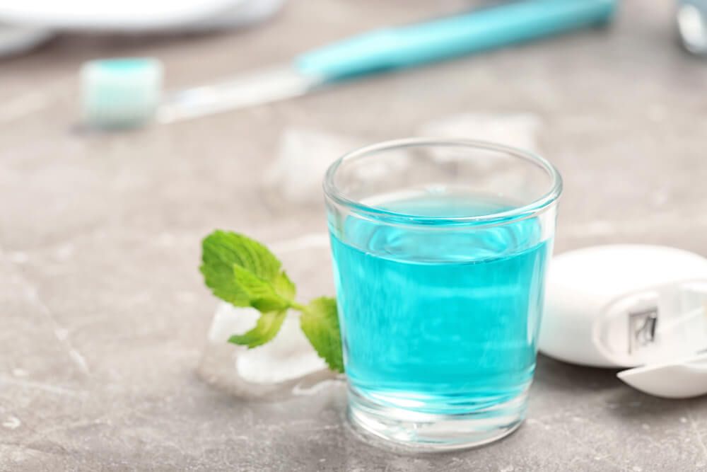 A glass full of mouthwash with flosser