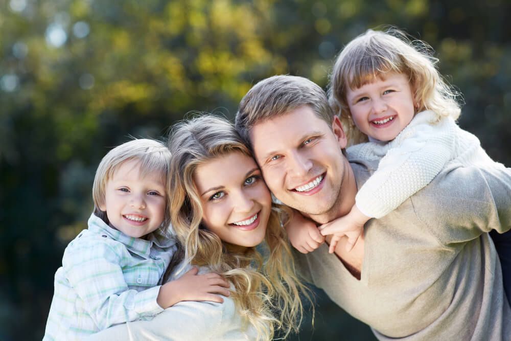 A family with white teeth smiling into the camera.