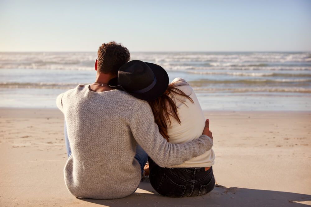 A couple sits together on a sandy beach.