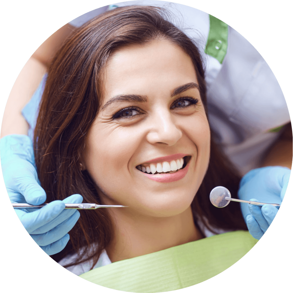 A woman smiling into the camera as a dentist stands behind her with examination tools.