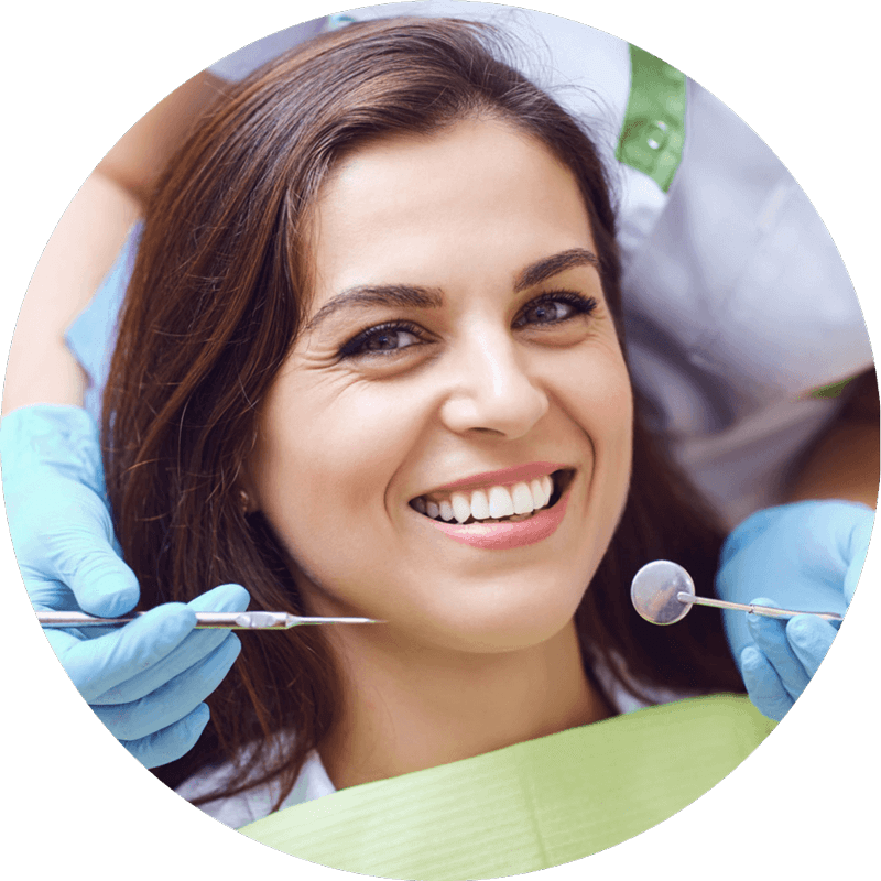 A woman smiling into the camera as a dentist stands behind her with examination tools.