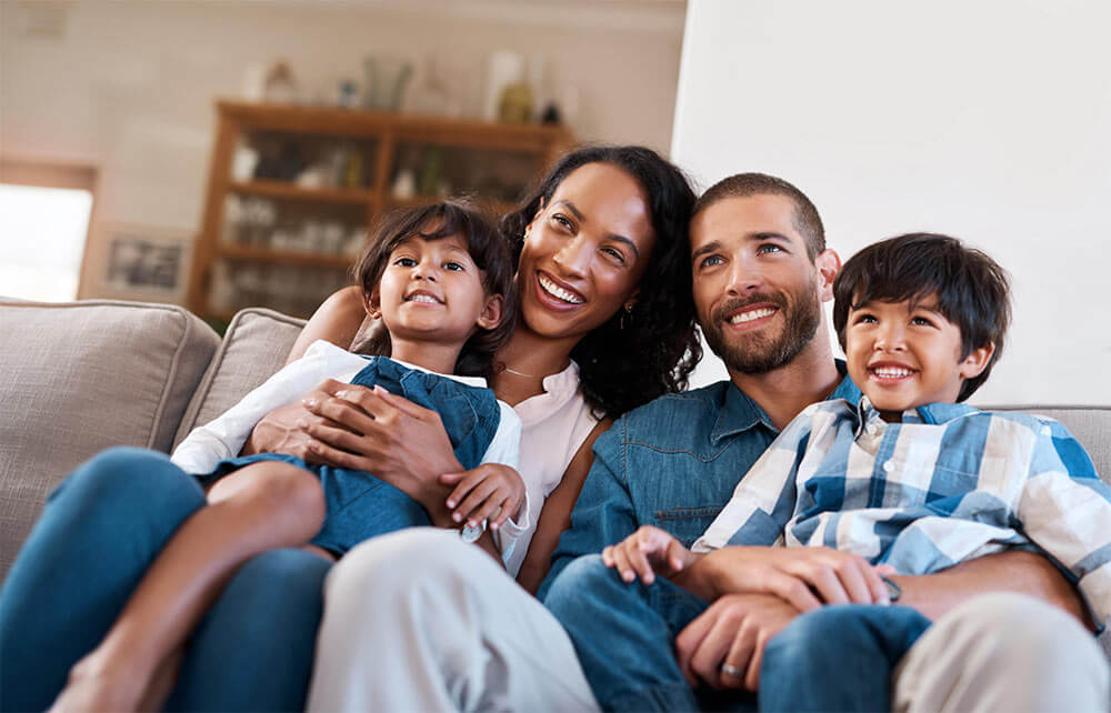 A smiling family sits on the couch together.