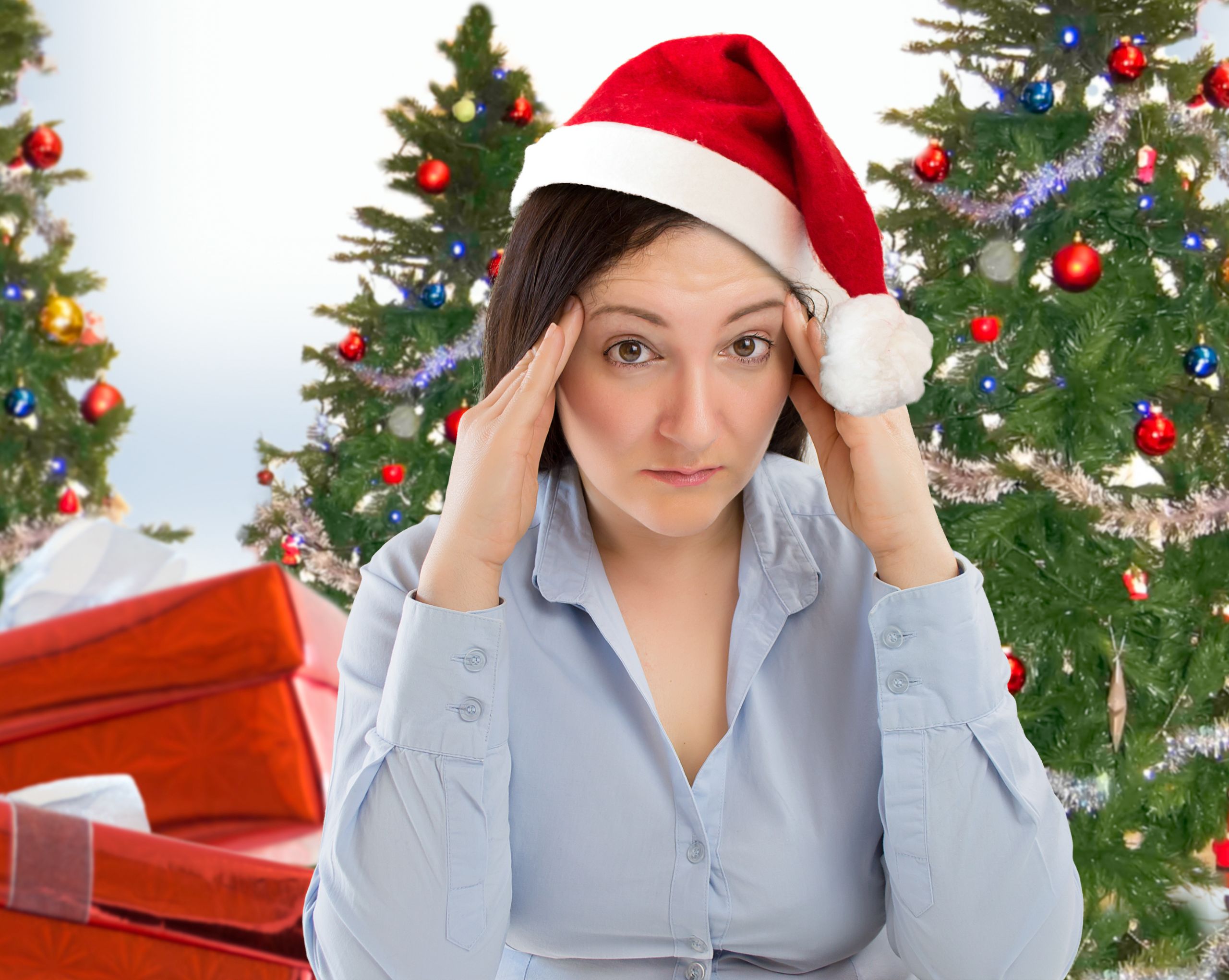 Stressed looking woman in a Santa hat in front of a Christmas tree