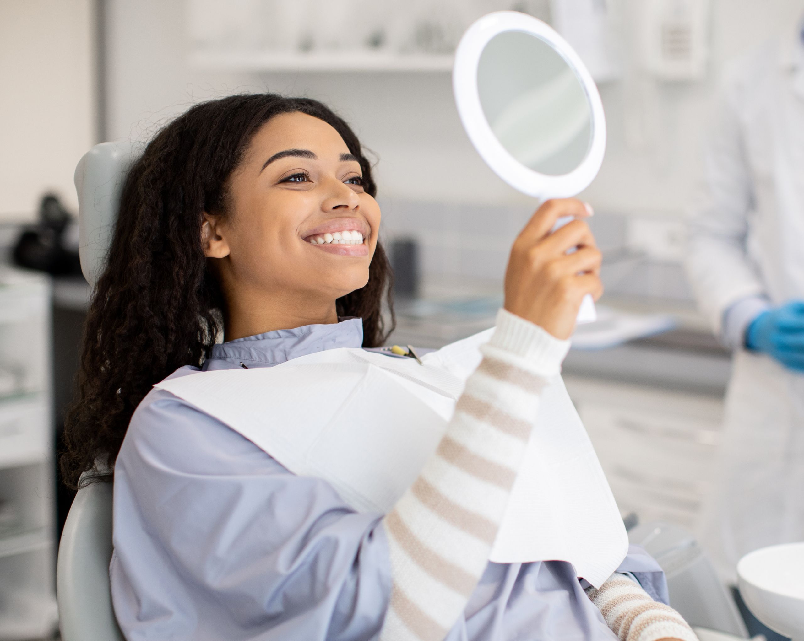 Young woman in dental chair admiring her new smile in a mirror