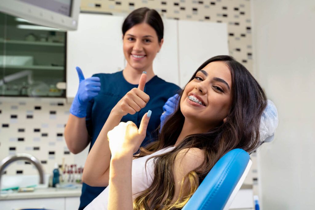 Beautiful young woman with dental braces sitting in dentist chair