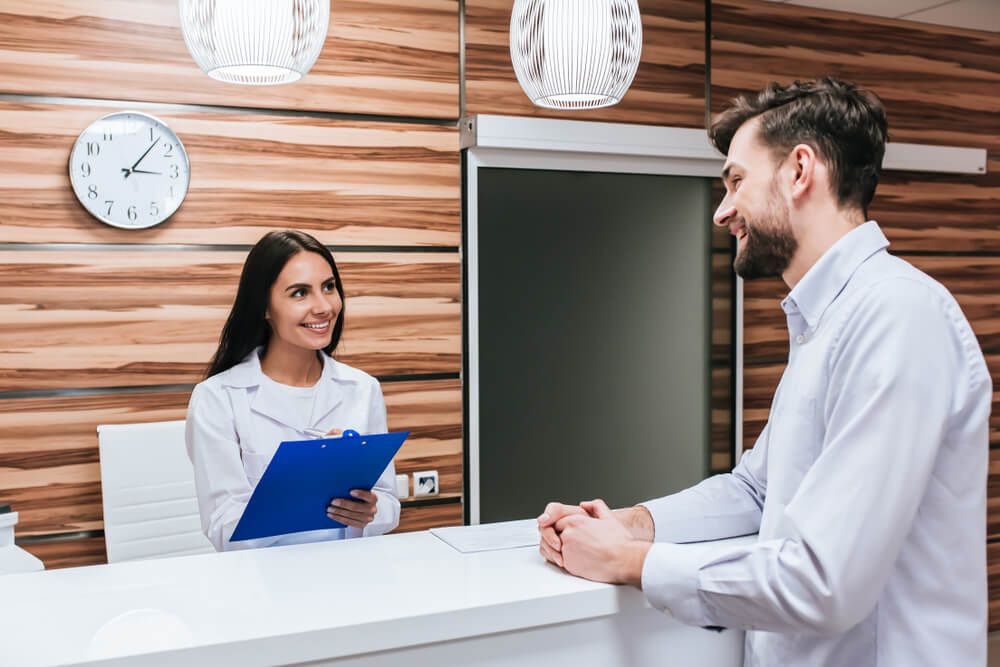 Young female doctor and handsome patient are standing on reception desk