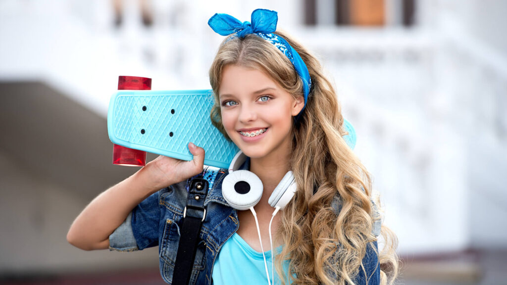 Cool girl with headphones and skateboard in city. Healthy, beautiful smile