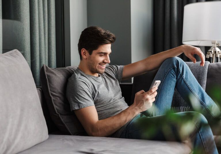 Attractive smiling young bearded man wearing casual clothes sitting on a couch