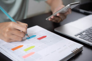 woman checking planner on mobile phone, taking note on calendar desk on office table