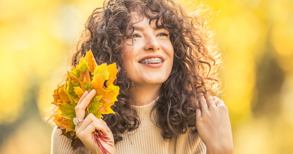 Young woman full of emotions from autumn season. Girl with a dental braces and curly hair.
