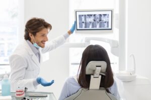 Handsome smiling dentist showing his patient x-ray results, on modern lcd display in modern dental office