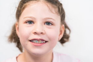 Little girl with rainbow braces smiling at the camera.