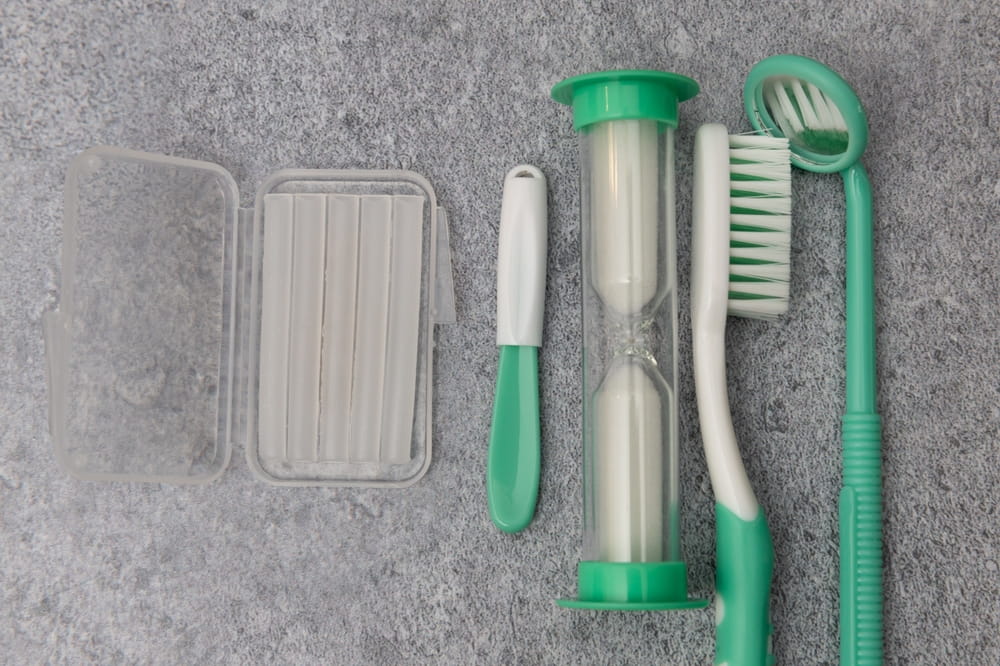 Orthodontics kit including wax, flosser, sand timer, toothbrush, and dental mirror on granite counter