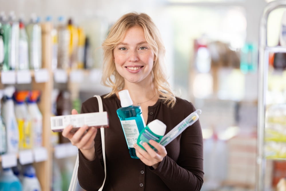 Positive beautiful young woman choosing toothpaste and oral care products in large store