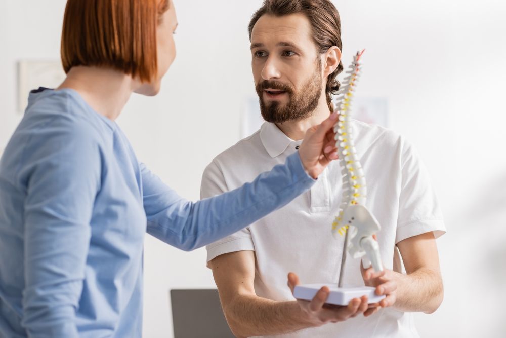 osteopath holding spine model and talking to woman in consulting room