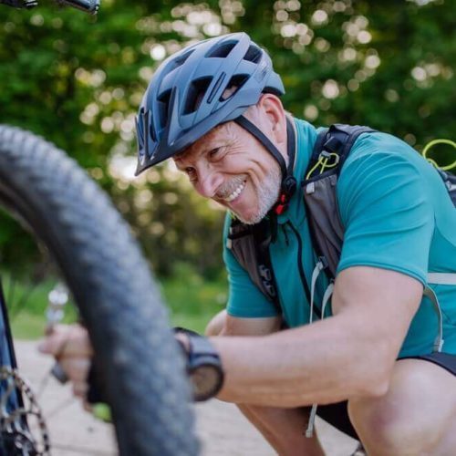 Active senior man repairing bicycle, pumping up tire in nature in summer.