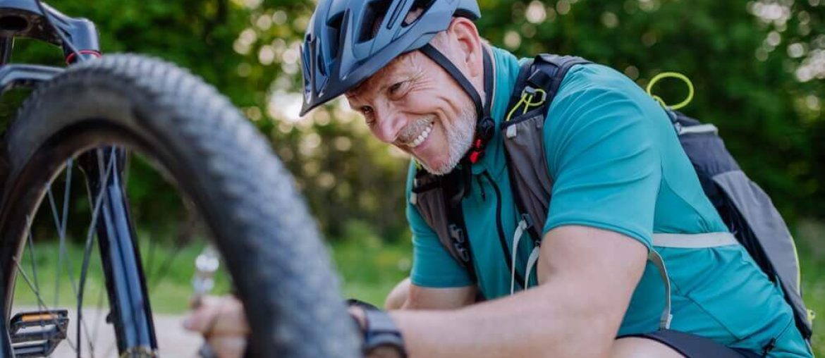 Active senior man repairing bicycle, pumping up tire in nature in summer.