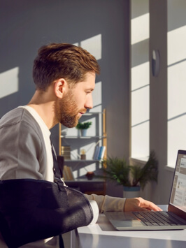 Man with broken arm working on laptop computer