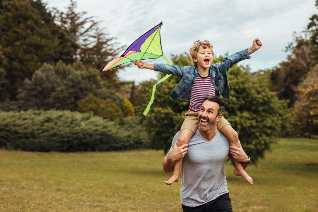 Father carrying son playing with kite in park