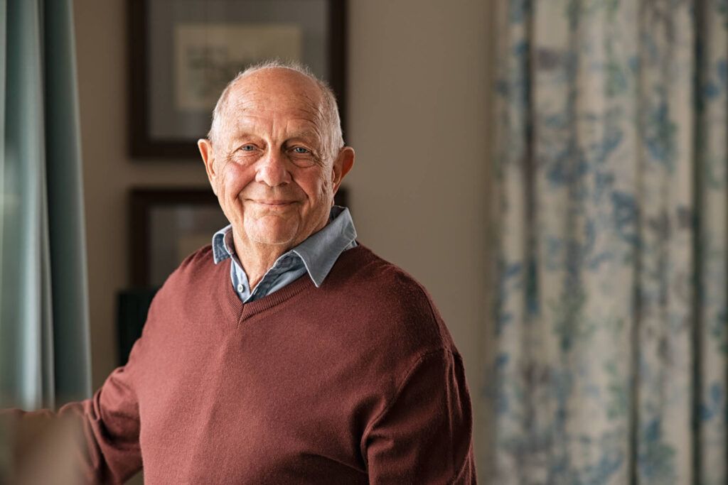 Portrait of happy retired senior man standing at home near window