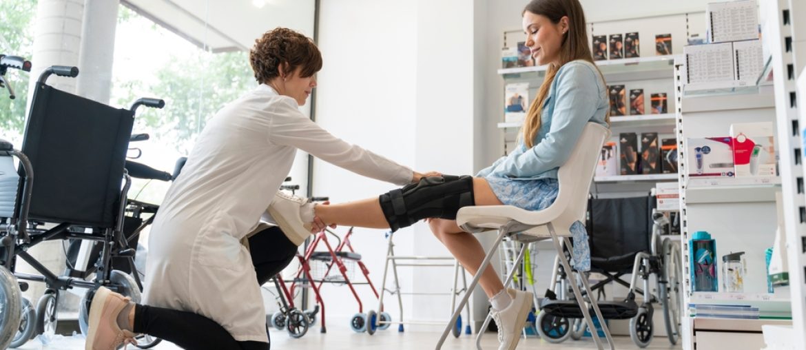 Orthopedist,Woman,Putting,A,Knee,Brace,On,A,Young,Client