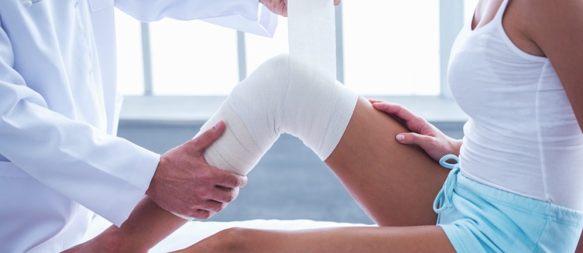 Cropped,Image,Of,Handsome,Doctor,Bandaging,Woman's,Injured,Knee,While