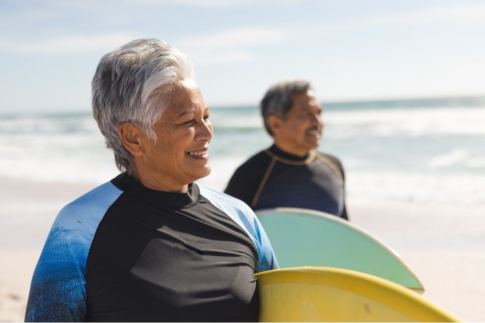 Smiling senior woman carrying surfboard with man at beach