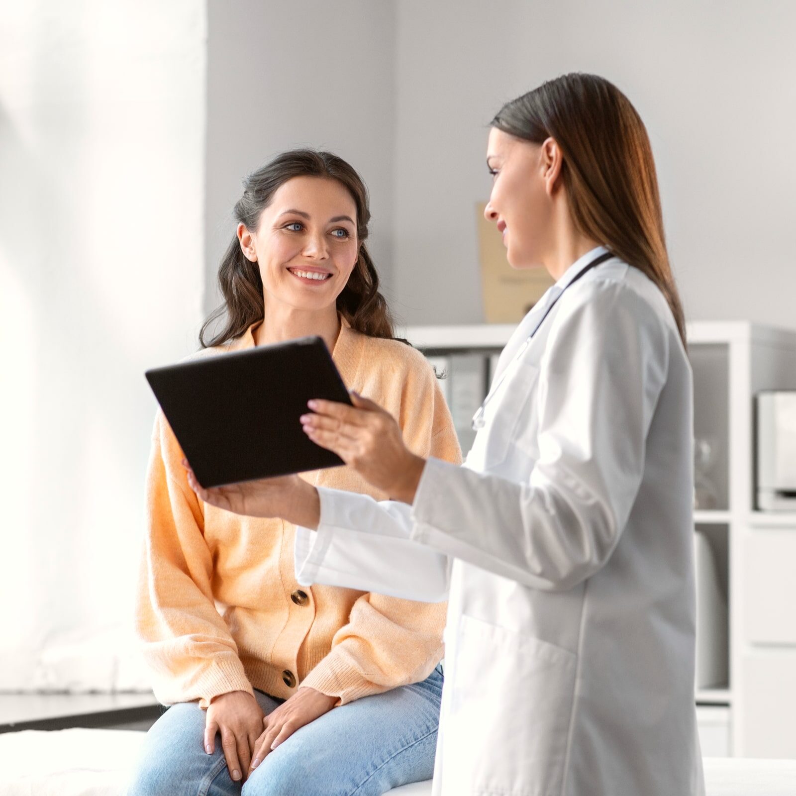 female doctor with tablet pc computer talking to smiling woman patient at hospital