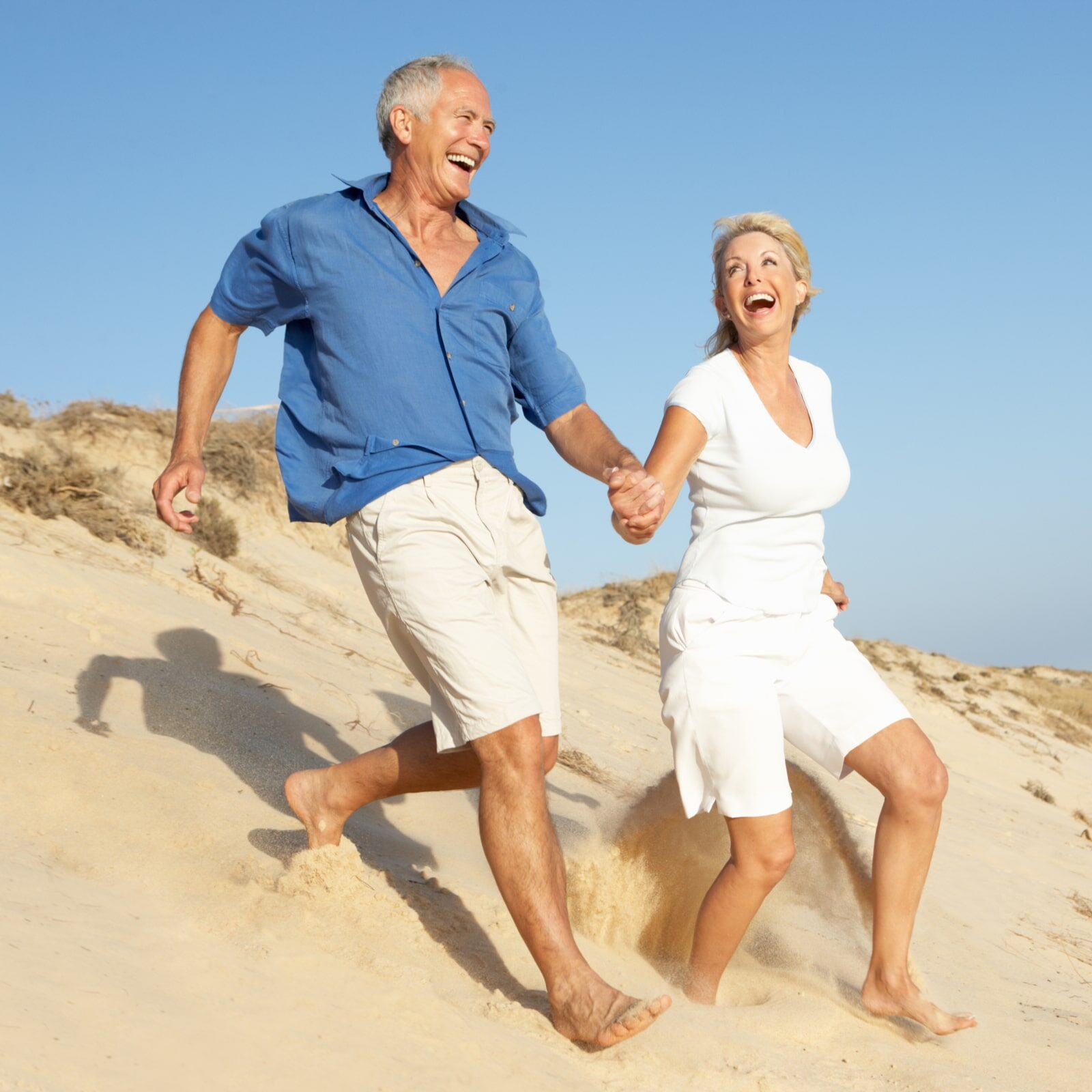 Senior Couple Enjoying Beach Holiday Running Down Dune