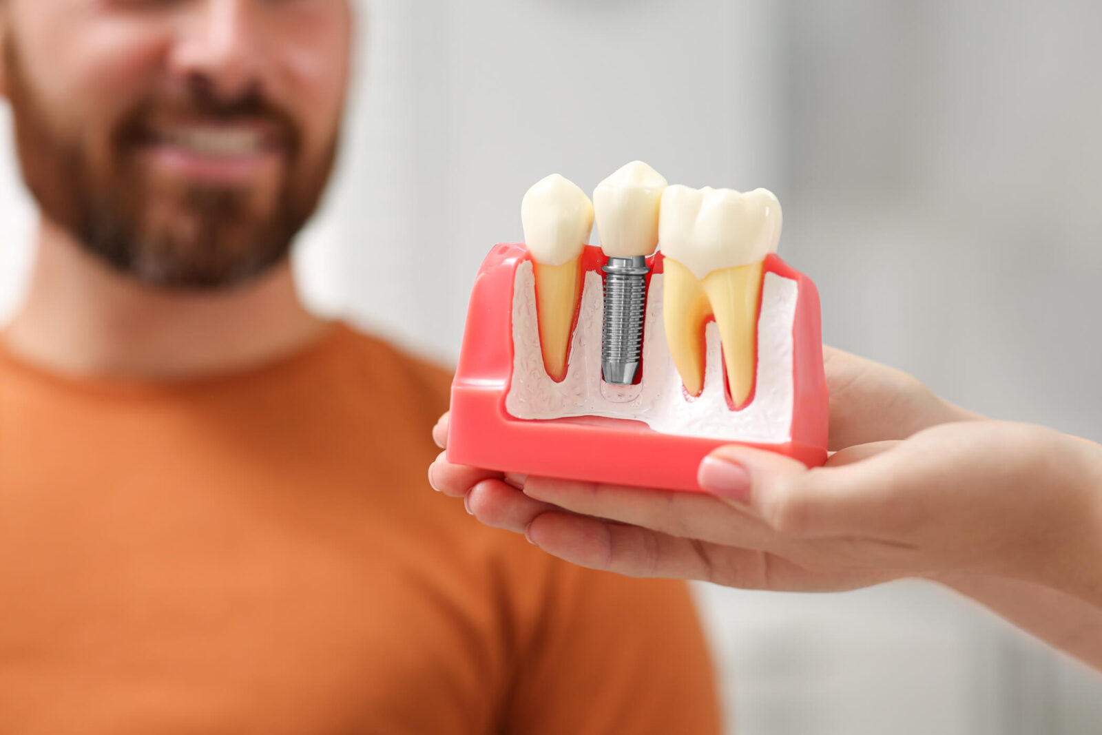 Doctor with educational model of dental implant consulting patient in clinic,