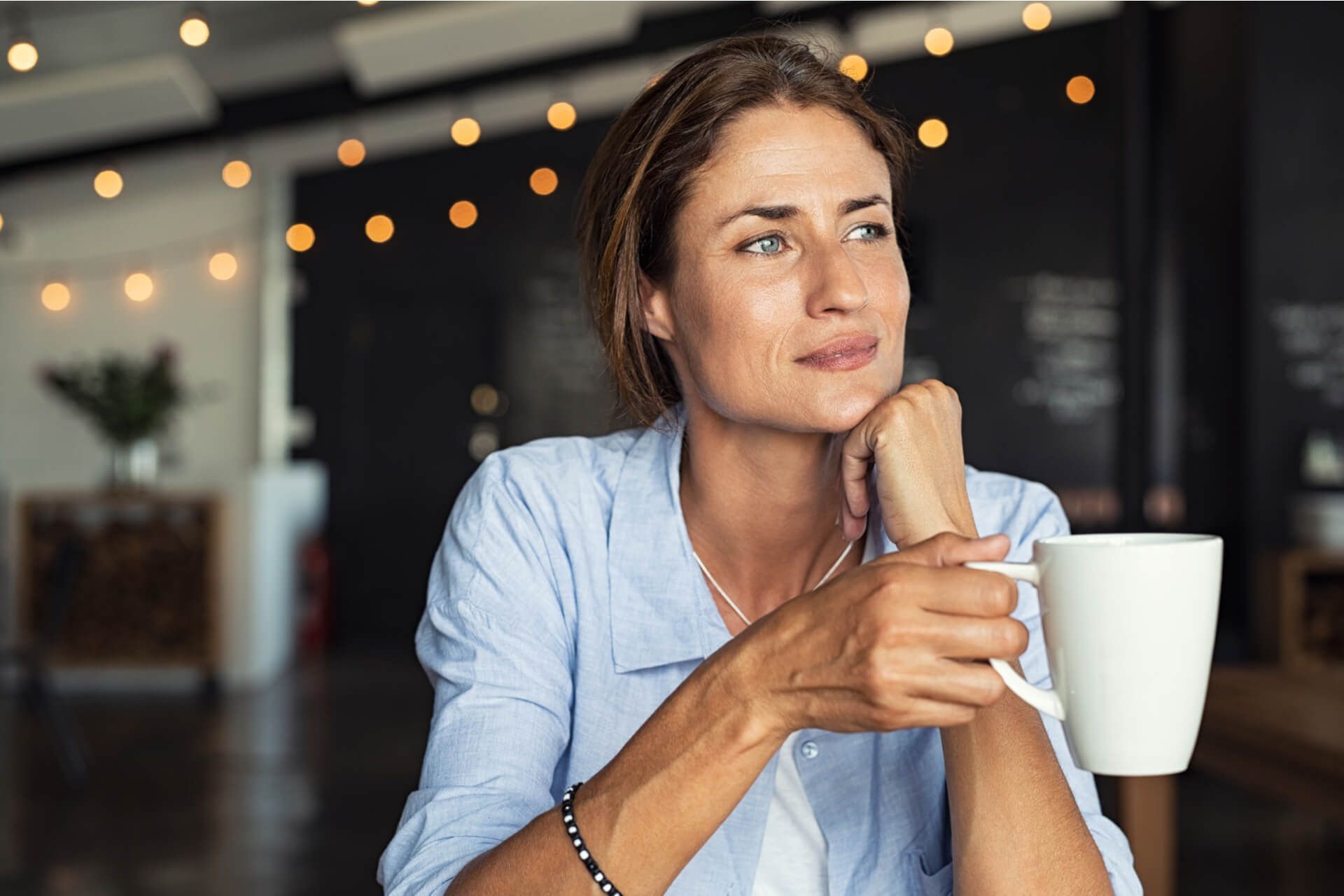 Thoughtful mature woman sitting in cafeteria holding coffee mug